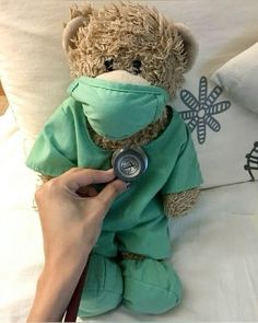 a person is holding a stethoscope to a teddy bear on a bed