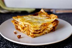 a white plate topped with lasagna on top of a black counter next to a knife and fork