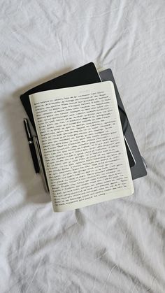 an open book sitting on top of a bed next to a pen and tablet computer