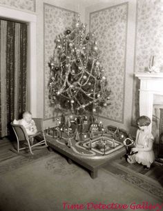 an old black and white photo of a child sitting in front of a christmas tree