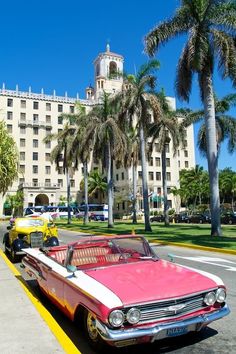 an old pink and white car is parked in front of a building with palm trees