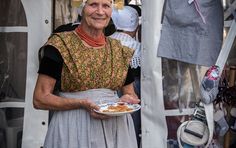 an older woman holding a plate of food in front of some clothes hanging on a line