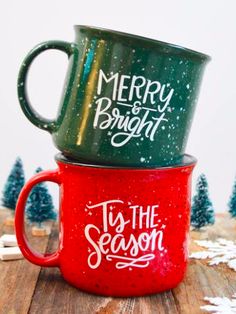 two green and red coffee mugs sitting on top of each other in front of snow covered trees