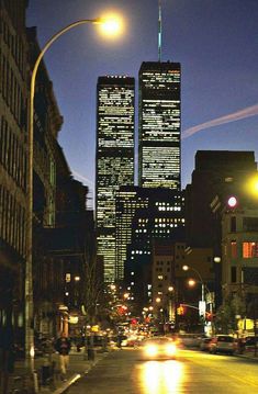 a city street at night with skyscrapers lit up in the background and cars driving on the road