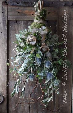 a wreath hanging on the side of a wooden door with greenery and dried flowers