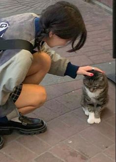 a girl petting a cat on the street while wearing a backpack and holding it in her hand