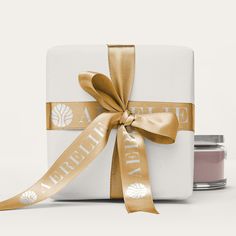 a wrapped gift box with a gold ribbon around it and two jars of jam in the background