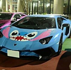 some cars are parked in front of a building with fake teeth on the hoods