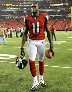 a football player is walking on the field with his helmet and glove in hand while holding a ball