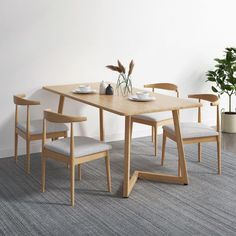 a dining table with four chairs and a plant in the corner next to it on a carpeted floor