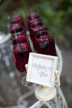 there are many glasses with red liquid in them on the glass stand and one has a sign that says raspberry pie