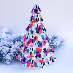 a paper christmas tree sitting on top of a white table next to snow covered branches