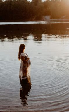 a pregnant woman standing in the middle of a body of water with trees in the background