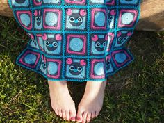 a person standing in the grass with their feet propped up on a bench wearing a crocheted blanket