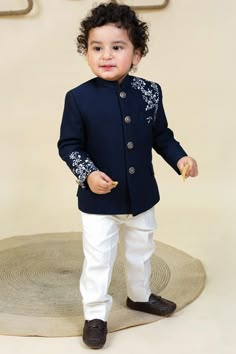 a little boy standing on top of a rug wearing a blue jacket and white pants