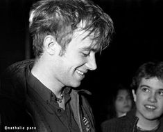 black and white photograph of two men smiling at each other while one man looks on