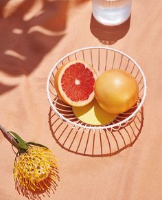 two grapefruits and an orange in a bowl on a table with a flower