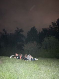 group of people laying in the grass at night with dark sky behind them and trees