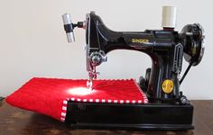 an old sewing machine sitting on top of a wooden table next to a red blanket