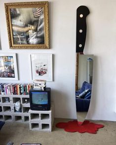 a large knife sticking out of the side of a wall next to a tv and bookshelf