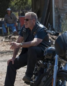 a man sitting on top of a motorcycle next to another person in the background with other people behind him