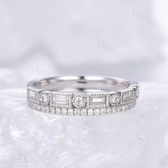 a white gold wedding band with baguetts and diamonds on it, sitting on a piece of ice