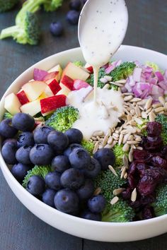 a white bowl filled with broccoli, blueberries, apples and other fruits