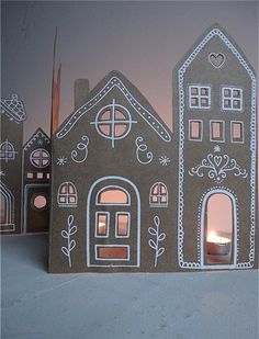 three cardboard houses with lit candles in the windows and one has a house on it