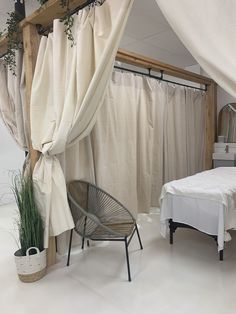 a bed and chair in a room with curtains on the wall, plants next to it