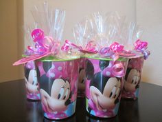 three plastic cups with minnie mouse designs and pink bows on the top, sitting on a table