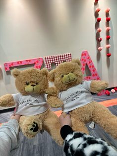 two brown teddy bears sitting next to each other in front of a wall with letters