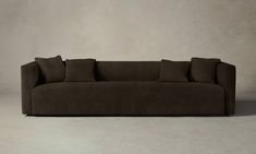 a brown couch sitting on top of a white floor next to a wall with two pillows