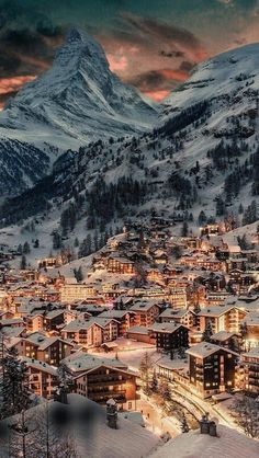 a town in the mountains covered in snow at night with lights shining on it's buildings