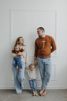 a man, woman and child are standing in front of a white wall holding hands