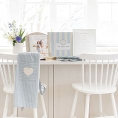 two white chairs sitting next to a table with a book on top of it and a vase filled with flowers