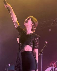 a woman standing on top of a stage with her arms in the air and holding a microphone