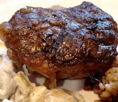 a piece of steak with mushrooms and gravy on a white plate next to mashed potatoes