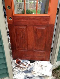 an orange front door with glass panes on the top and bottom, is surrounded by debris