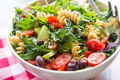 a white bowl filled with pasta salad on top of a checkered table cloth next to a fork and knife