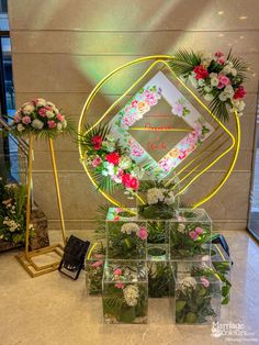 flowers and greenery are arranged on display in front of a wall with a gold frame