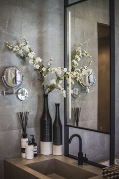 a bathroom sink sitting under a large mirror next to a vase with flowers in it