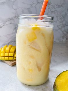 a mason jar filled with yellow liquid next to sliced pineapples and a mango