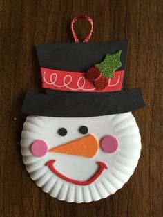 a paper plate with a snowman face on it and a holly berry decoration hanging from the top