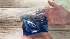 a hand holding a blue bag filled with plastic material on top of a wooden table