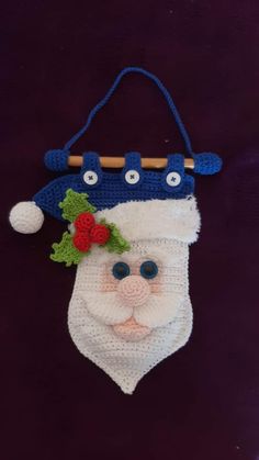 a crocheted christmas stocking hanging from a wooden stick on a purple background