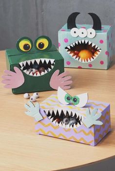 two paper boxes with fake mouths and eyes on top of a wooden table next to each other