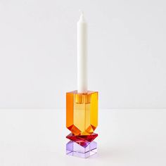 an orange candle holder with a white candle in it on top of a plain surface