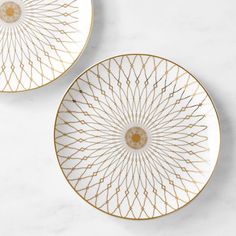 two white and gold plates sitting on top of a marble countertop next to each other