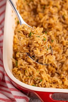 a spoon full of rice in a red and white casserole dish on a checkered cloth