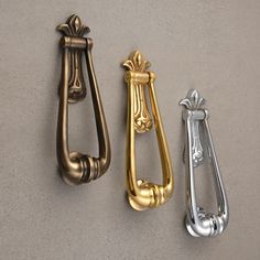 three brass and silver door handles on a gray wall, one with an ornate handle